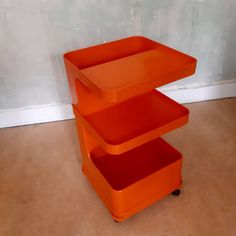 an orange three tiered shelf sitting on top of a hard wood floor next to a wall