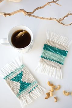 a cup of coffee and two knitted coasters next to some cashews