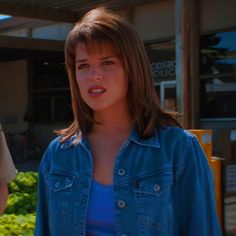 a woman standing next to a man in a blue shirt and jean jacket on the street