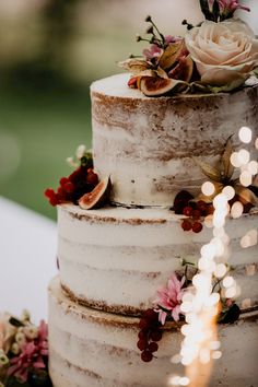 a three tiered cake with flowers and fruit on the top is sitting on a table