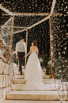 a bride and groom walking down the stairs at their outdoor wedding ceremony with fairy lights all around them