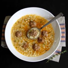 a white bowl filled with soup and meatballs on top of a cloth next to a spoon