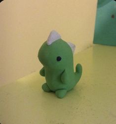 a small green toy sitting on top of a counter next to a blue object with a white bow