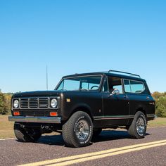 an old ford bronco is parked on the side of the road with trees in the background