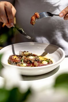 a person eating food from a white plate with silver utensils in their hands