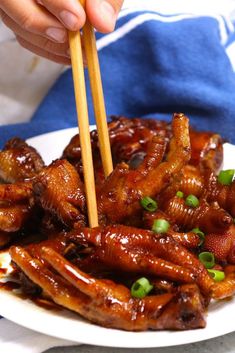 a person holding chopsticks over some food on a white plate with green onions