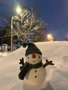 a snowman with a hat and scarf on standing in the snow at night time