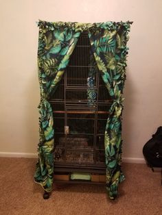 a bird cage with a curtain over it that has leaves on the top and bottom