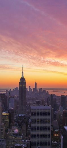 the sun is setting over new york city, with skyscrapers in the foreground