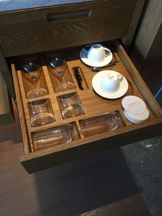 an open drawer with glasses, plates and cups in it on a wooden table top