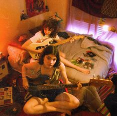 two young women sitting on the floor playing guitars in a room with other furniture and decorations