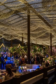 people are sitting at tables in a large room with lights on the ceiling and flowers all around