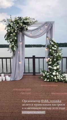 an outdoor wedding set up with white flowers and greenery on the ground next to water