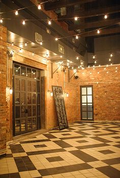 an empty room with black and white checkered flooring, lights strung from the ceiling