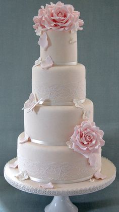 a three tiered wedding cake with pink flowers on top and white lace trimmings