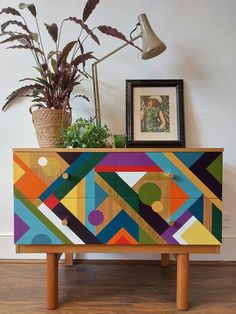 a wooden cabinet with an abstract design painted on the front and sides, next to a potted plant