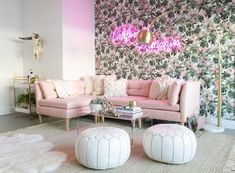 a living room with pink couches and white poufces on the floor, in front of a floral wallpaper