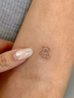 a small teddy bear tattoo on the wrist