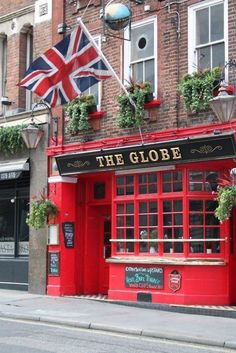 a red building with potted plants on the outside and an union jack flag hanging above it