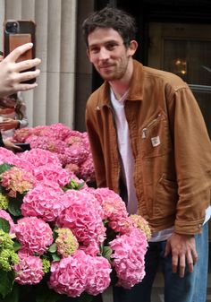 a man standing next to a large bouquet of pink and green flowers with a cell phone in his hand