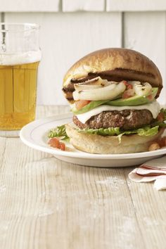 a hamburger with onions, lettuce and tomato on a white plate next to a napkin