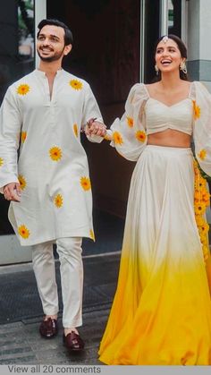 two people dressed in white and yellow are walking down the street holding each other's hands