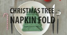 a christmas tree napkin folded on a plate with silverware and candy canes next to it