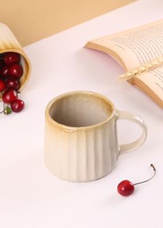 a white cup with some cherries in it next to an open book and a cherry