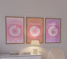 two pink posters hang on the wall above a white dresser with a lamp next to it