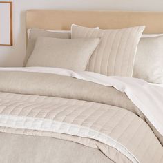 a bed with white sheets and pillows in a bedroom next to a framed picture on the wall