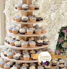 a three tiered cake with cupcakes on the side and flowers in the background