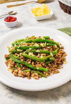 a white plate topped with asparagus covered in meat and seasoning next to lemon wedges