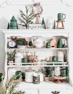 a white shelf filled with green and white christmas decor on top of a wooden table