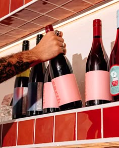 a man is holding two bottles of wine on a shelf with red tiles in the background