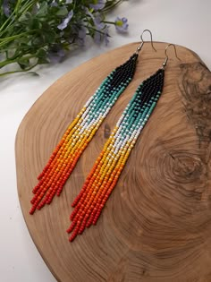 multicolored beaded earrings on wooden board next to flowers