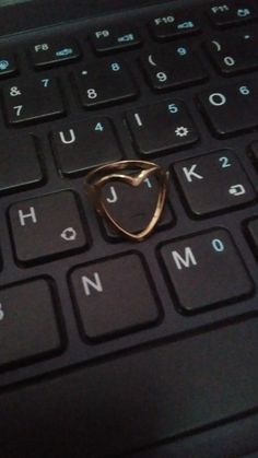 a gold ring sitting on top of a black keyboard with the word love spelled below it