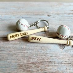 two baseball bat keychains with the word mustangs drawn on them are sitting on a wooden surface