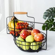 two metal baskets filled with fruit on top of a white table next to a potted plant