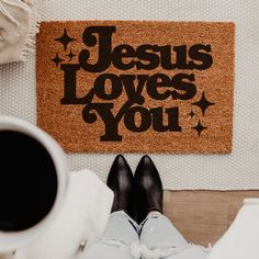 someone is sitting on the floor with their feet up in front of a door mat that says jesus loves you