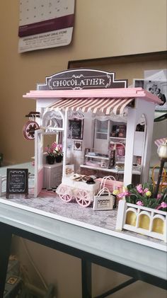 a miniature model of a chocolate shop with pink trimmings and flowers on display