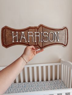 a person holding up a wooden sign with the word harrison on it in front of a crib