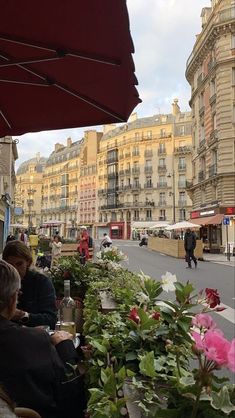 people are sitting at tables with umbrellas over them on the sidewalk in front of buildings