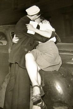 an old black and white photo of a sailor kissing a woman in front of a car