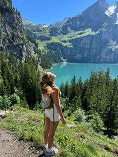 a woman standing on top of a lush green hillside next to a large body of water