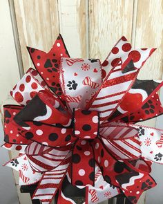 a red and black polka dot dog hair bow with paw prints on the front, attached to a wooden fence