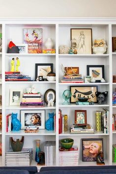 a living room filled with lots of books on top of a white book shelf next to a blue couch