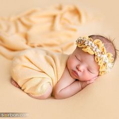 a baby sleeping on top of a blanket wearing a yellow headband with pearls in it's hair