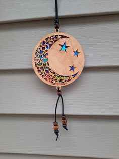 a wooden sun and moon decoration hanging on the side of a house with beads around it