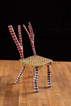 a chair made out of strips and sticks on top of a wooden table with black background