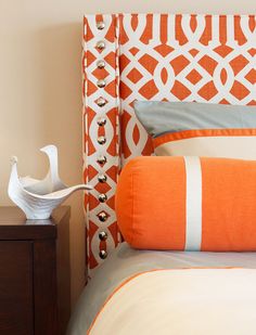 a bed with an orange and white headboard next to a night stand in a bedroom